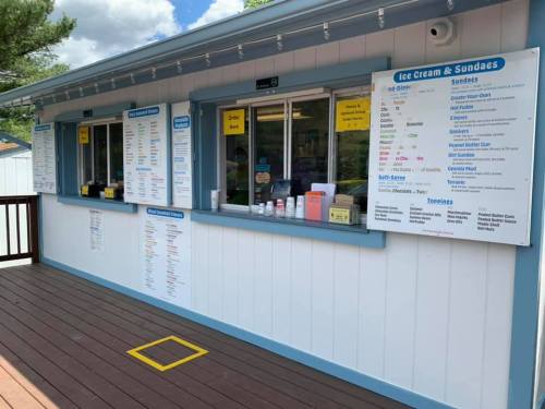 A colorful ice cream stand with menus for sundaes and toppings displayed on the wall, surrounded by a wooden deck.