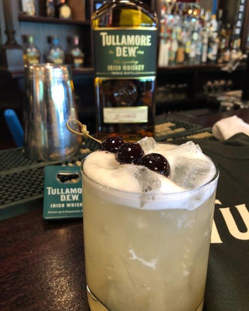 A cocktail with ice and cherries, featuring Tullamore Dew Irish whiskey in the background.