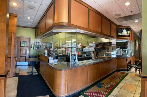 Interior of a restaurant featuring a service counter, glass display, and seating area with wooden accents.
