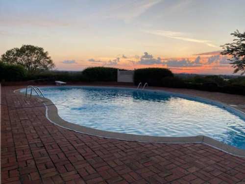 A serene swimming pool at sunset, surrounded by greenery and a brick patio.