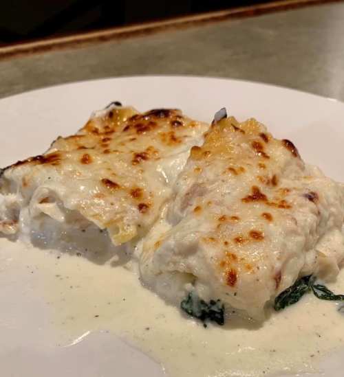 Two pieces of creamy spinach lasagna with a golden, bubbly cheese topping on a white plate.