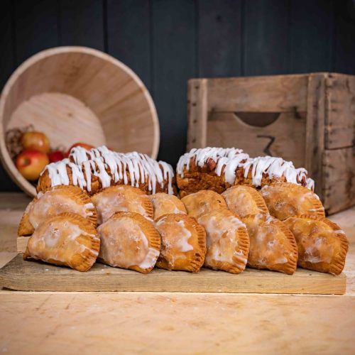 A display of glazed pastries and sweet rolls on a wooden board, with a rustic background of a basket and crate.