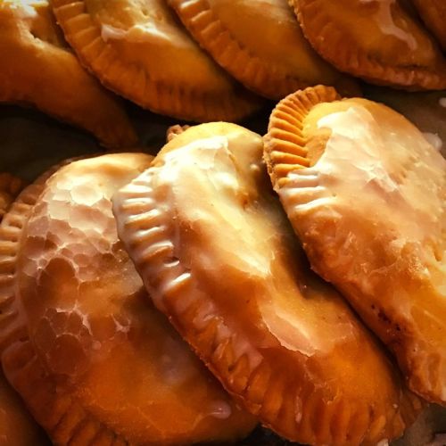A close-up of golden-brown pastries with a glossy glaze, stacked neatly on a tray.