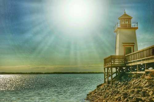 A lighthouse stands on a pier by the water, illuminated by bright sunlight and surrounded by a serene landscape.