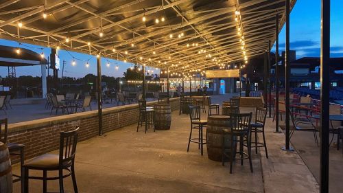 Outdoor dining area with string lights, empty tables, and chairs under a canopy at dusk.