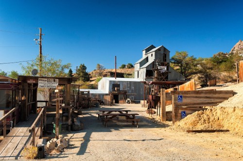 A rustic mining town with wooden structures, a large building, and a clear blue sky in the background.