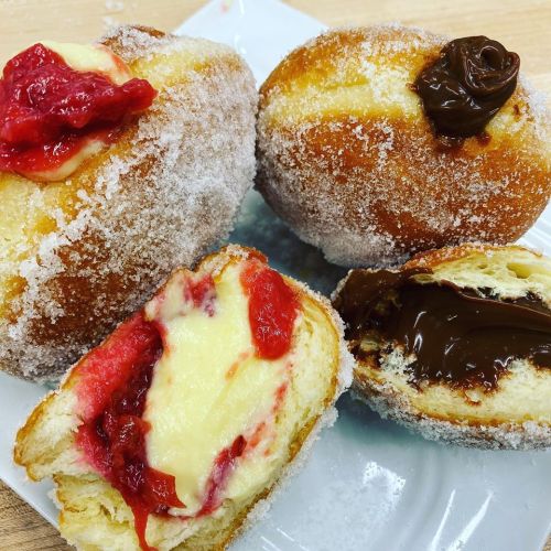 Four sugar-coated doughnuts, two filled with strawberry jam and cream, and two filled with chocolate hazelnut spread.