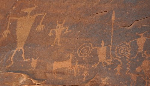 Petroglyphs depicting various figures, including humanoid shapes and animals, carved into a rocky surface.