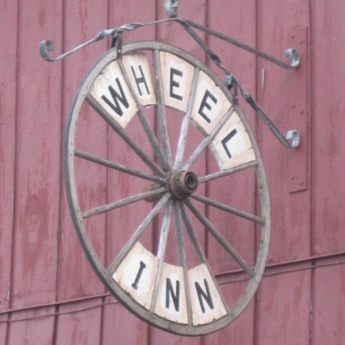 A rustic sign shaped like a wheel, displaying the words "WHEEL INN" in bold letters against a red background.