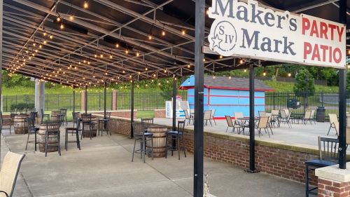Outdoor patio area with string lights, tables, and chairs, featuring a sign for Maker's Mark Party Patio.