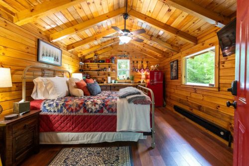 Cozy cabin interior featuring a bed, wooden walls, a red fridge, and a window with natural light.