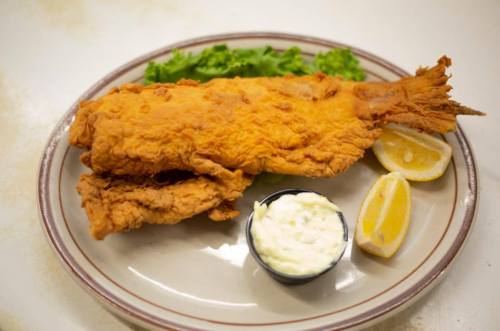 A plate with two pieces of fried fish, lettuce, lemon wedges, and a small bowl of tartar sauce.