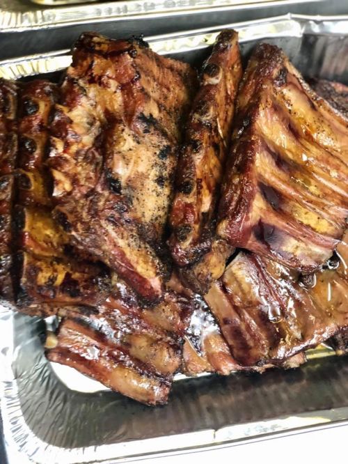 A close-up of a tray filled with grilled, smoky ribs, glistening with seasoning and sauce.