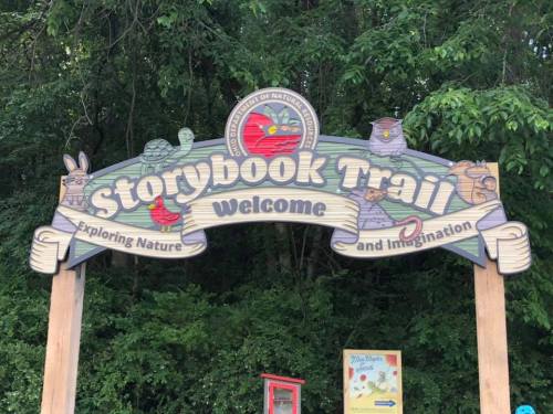 Sign for the Storybook Trail, featuring animals and nature-themed illustrations, welcoming visitors to explore.