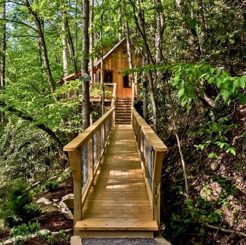 A wooden bridge leads to a cozy cabin nestled among lush green trees.