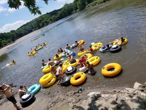 A group of people floating on colorful inner tubes in a river on a sunny day, with trees in the background.