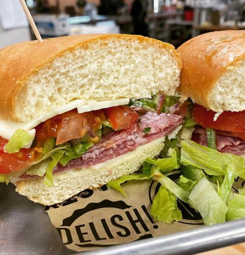A close-up of a sandwich with layers of lettuce, tomato, and deli meats, served on a soft bun.