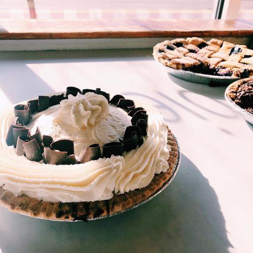 A chocolate cream pie topped with whipped cream and chocolate curls, with other desserts in the background.