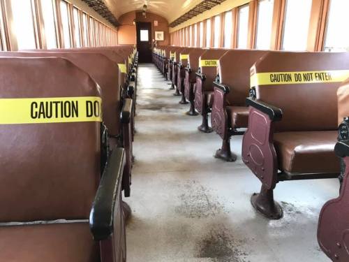 Interior of an empty train car with brown seats and yellow caution tape reading "Caution Do Not Enter."