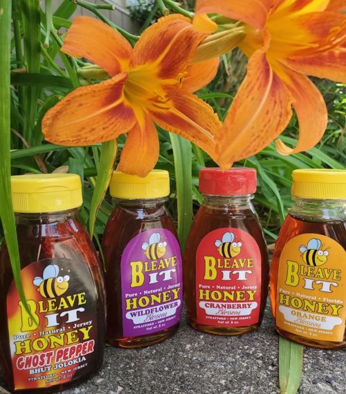 Four bottles of Bleave It honey in various flavors, with vibrant orange flowers in the background.
