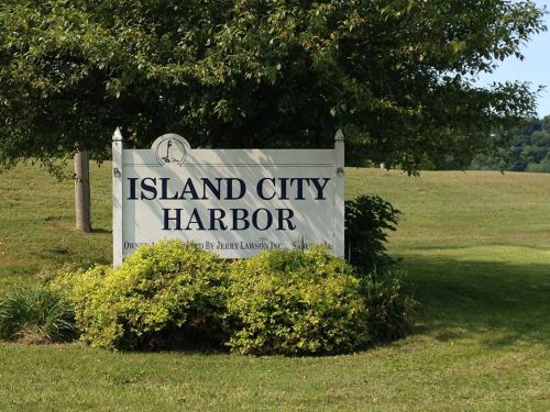 Sign for Island City Harbor surrounded by greenery, with a clear blue sky in the background.