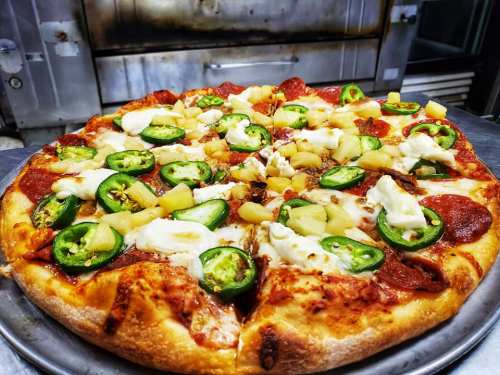 A freshly baked pizza topped with pepperoni, jalapeños, pineapple, and mozzarella cheese on a golden crust.