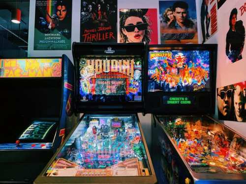 A vibrant arcade scene featuring pinball machines and retro posters on the wall, creating a nostalgic atmosphere.