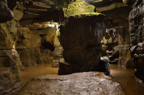 A dimly lit underground cave with rock formations and shallow water reflecting the surroundings.