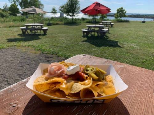 A serving of nachos topped with cheese, salsa, jalapeños, and sour cream, with a scenic outdoor picnic area in the background.