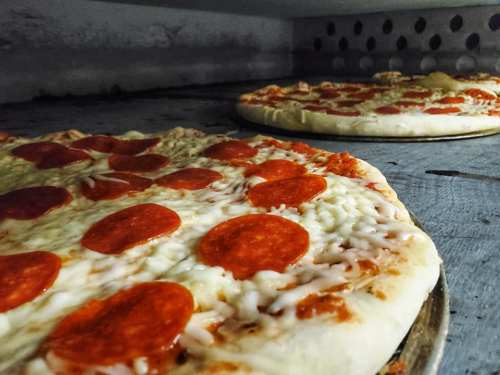 Two pizzas with melted cheese and pepperoni slices baking in an oven.