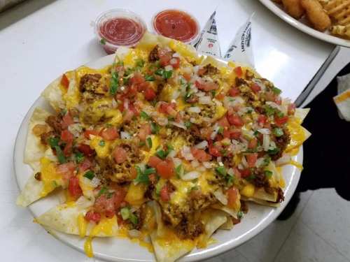 A plate of nachos topped with cheese, ground meat, diced tomatoes, onions, and green onions, served with salsa.