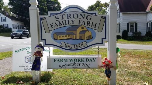 Sign for Strong Family Farm, established 1878, announcing Farm Work Day on September 20th, with scarecrows nearby.