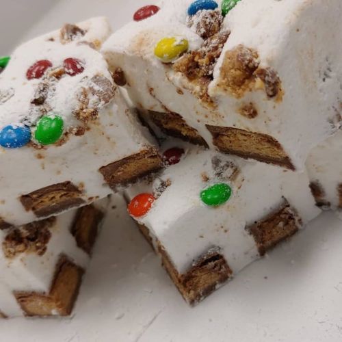 Close-up of stacked marshmallow treats with colorful candy pieces and a chocolate layer inside.