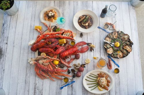 A vibrant seafood feast featuring lobsters, oysters, shrimp, and sides, arranged on a rustic wooden table.
