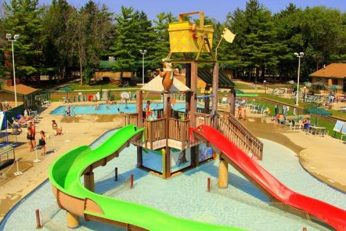 A colorful water park with slides, a splash pad, and people enjoying the sunny day surrounded by trees.