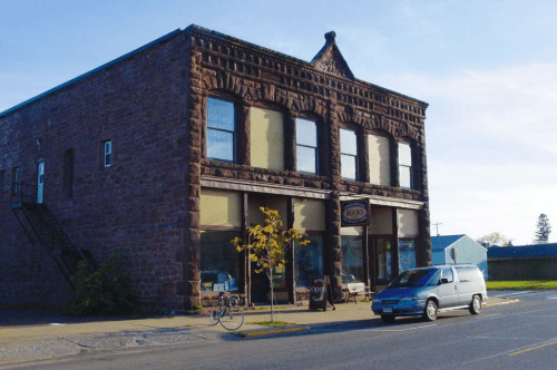 Historic stone building with large windows, a bicycle parked outside, and a tree in front on a quiet street.