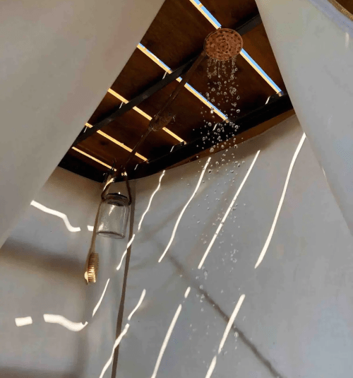A showerhead with water droplets falling, viewed from inside a tent with light filtering through the fabric.