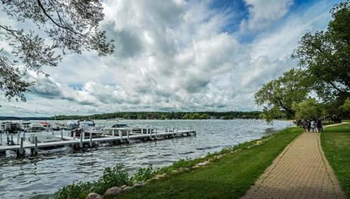 A scenic lakeside view with boats docked, a grassy path, and dramatic clouds in the sky.