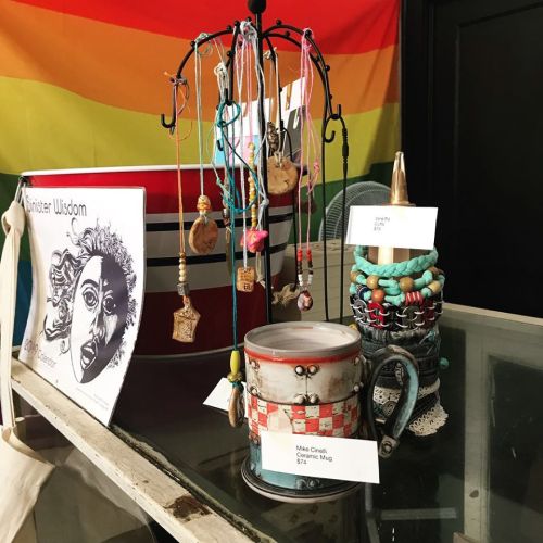 A display of handmade jewelry and crafts, including bracelets and a decorated mug, against a colorful background.
