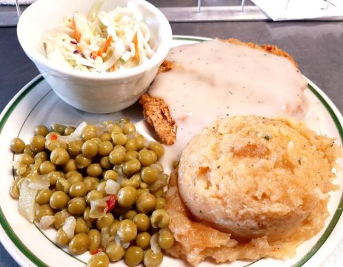 A plate of fried chicken with gravy, mashed potatoes, green peas, and a side of coleslaw.