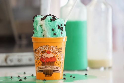 A colorful ice cream cup with mint and chocolate chip flavors, surrounded by bottles of green and white liquids.