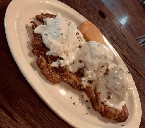 A plate of fried chicken topped with creamy white gravy, served with a biscuit on the side.