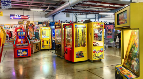 Colorful arcade with various game machines, including claw machines and ticket redemption games, in a lively setting.