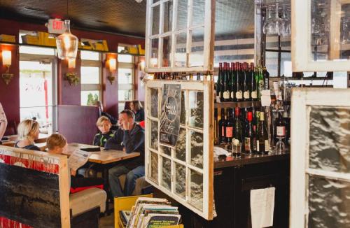 A cozy restaurant interior with a bar displaying wine bottles and patrons seated at tables.