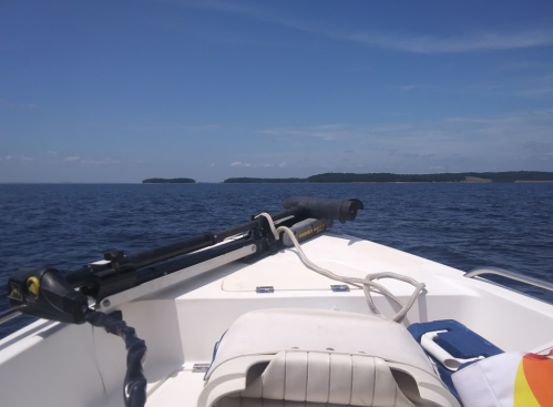 View from the bow of a boat on calm water, with distant islands and a clear blue sky.