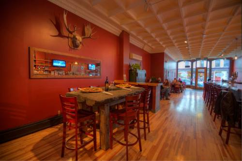 Cozy restaurant interior with red walls, wooden tables, and a mounted deer head, featuring a bar and seating area.