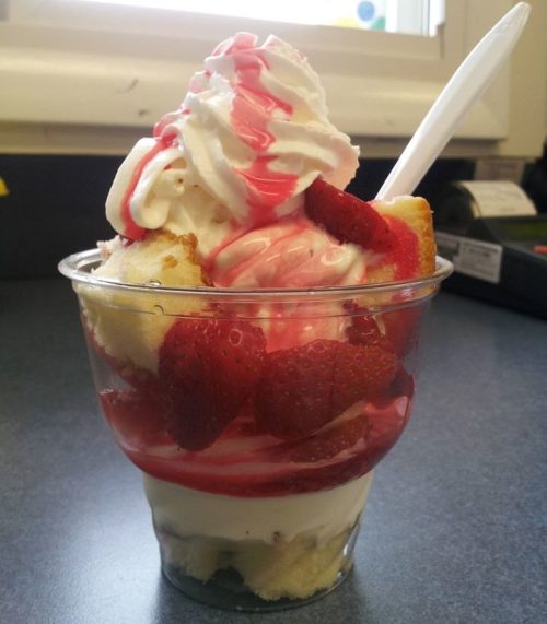 A dessert cup filled with layers of cake, strawberries, whipped cream, and strawberry sauce.