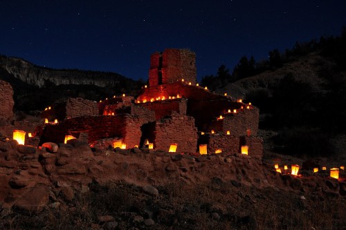 Ancient stone ruins illuminated by lanterns at night, under a starry sky.