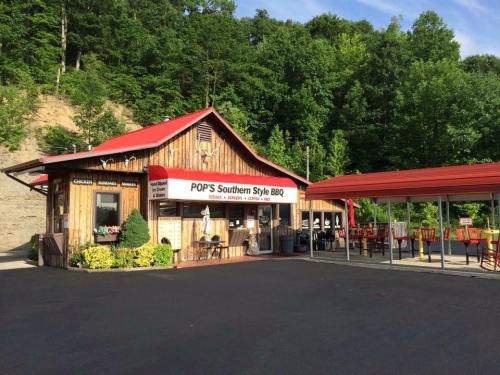 A rustic BBQ restaurant with a wooden exterior and red roof, surrounded by greenery and outdoor seating.