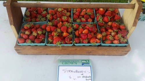 A wooden display of fresh strawberries in green baskets, with a sign reading "Strawberries $6.00 per quart."